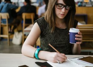 A female student writing a paper with coffee cup in hand.